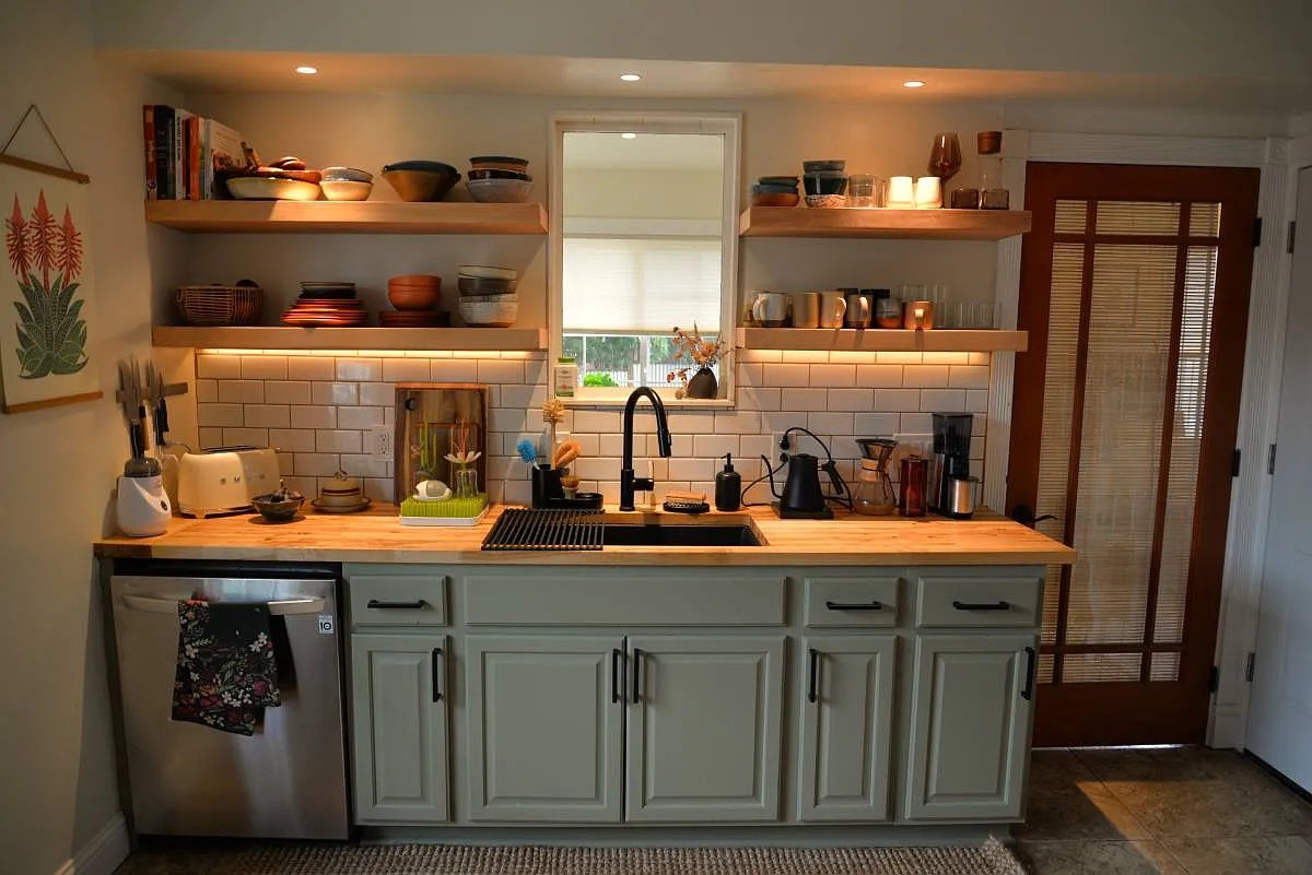 Kitchen after renovation with open shelving, subway tile, and sage cabinets